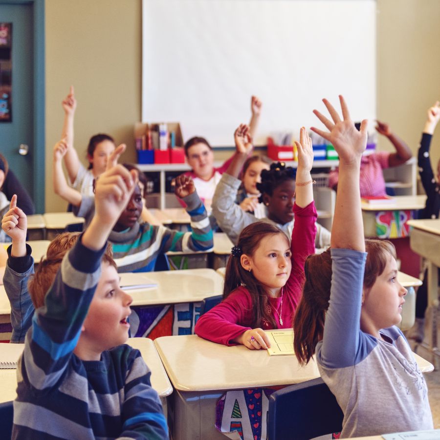 happy children raising hands in the classroom