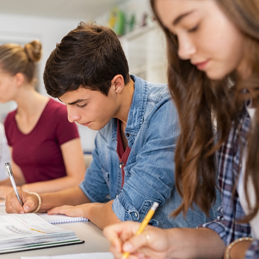 high school students writing at a table in a classroom
